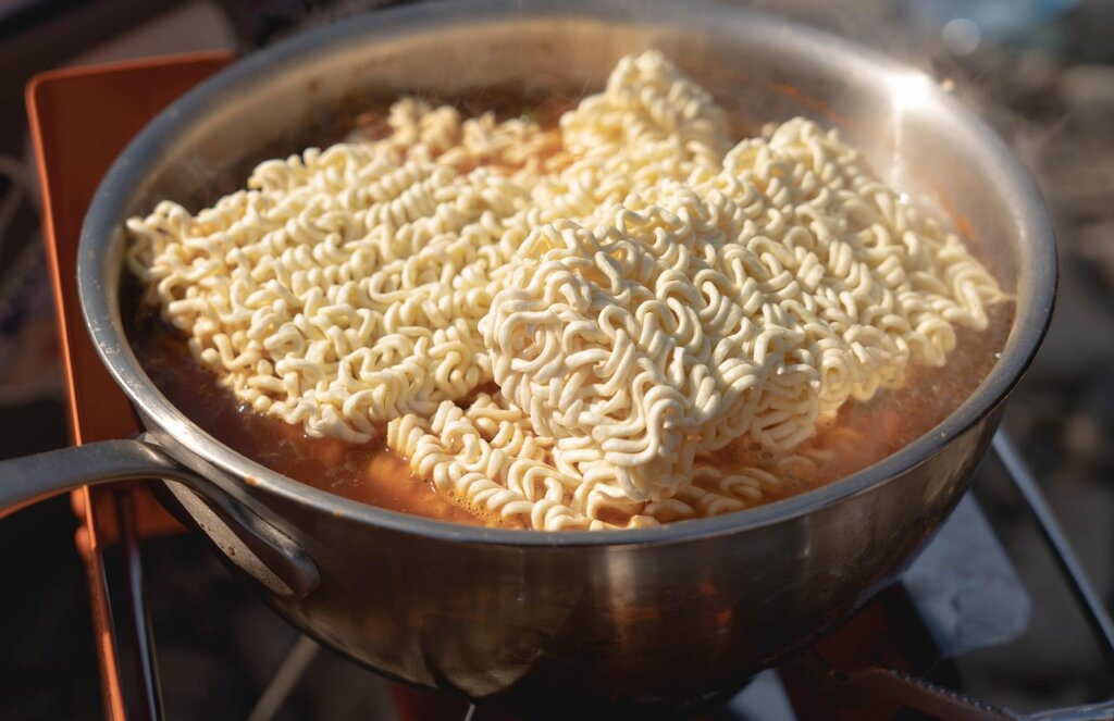 ramen noodles being dropped into boiling water in a pot